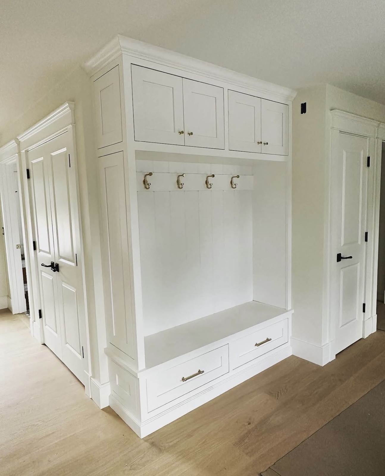 White custom mudroom cabinetry with bench and brass hooks